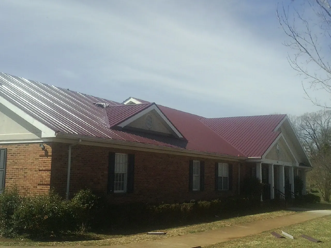 Red metal roof with gabled entries on a long brick building, from a Hail Damage Roof Repair job in Allyn