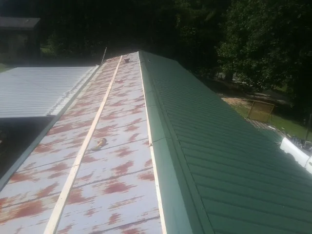 Old rusted panels beside newly installed green metal roofing — Wind Damage Roof Repair by Roofing Brothers in Allyn