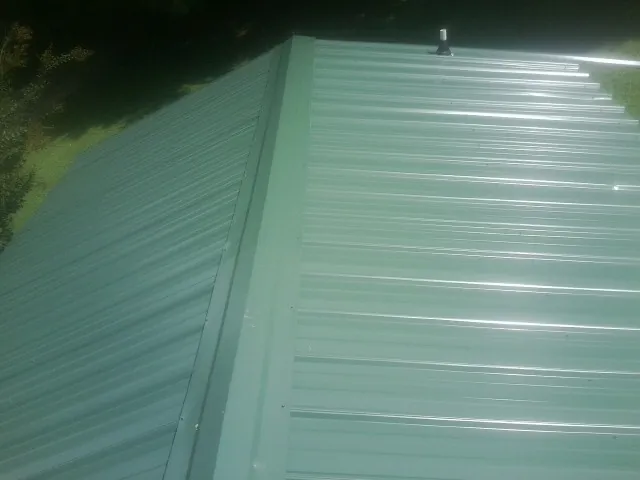 New green metal panels meeting at the ridge of a roof — Flat Roof Repair work by our crew in Allyn
