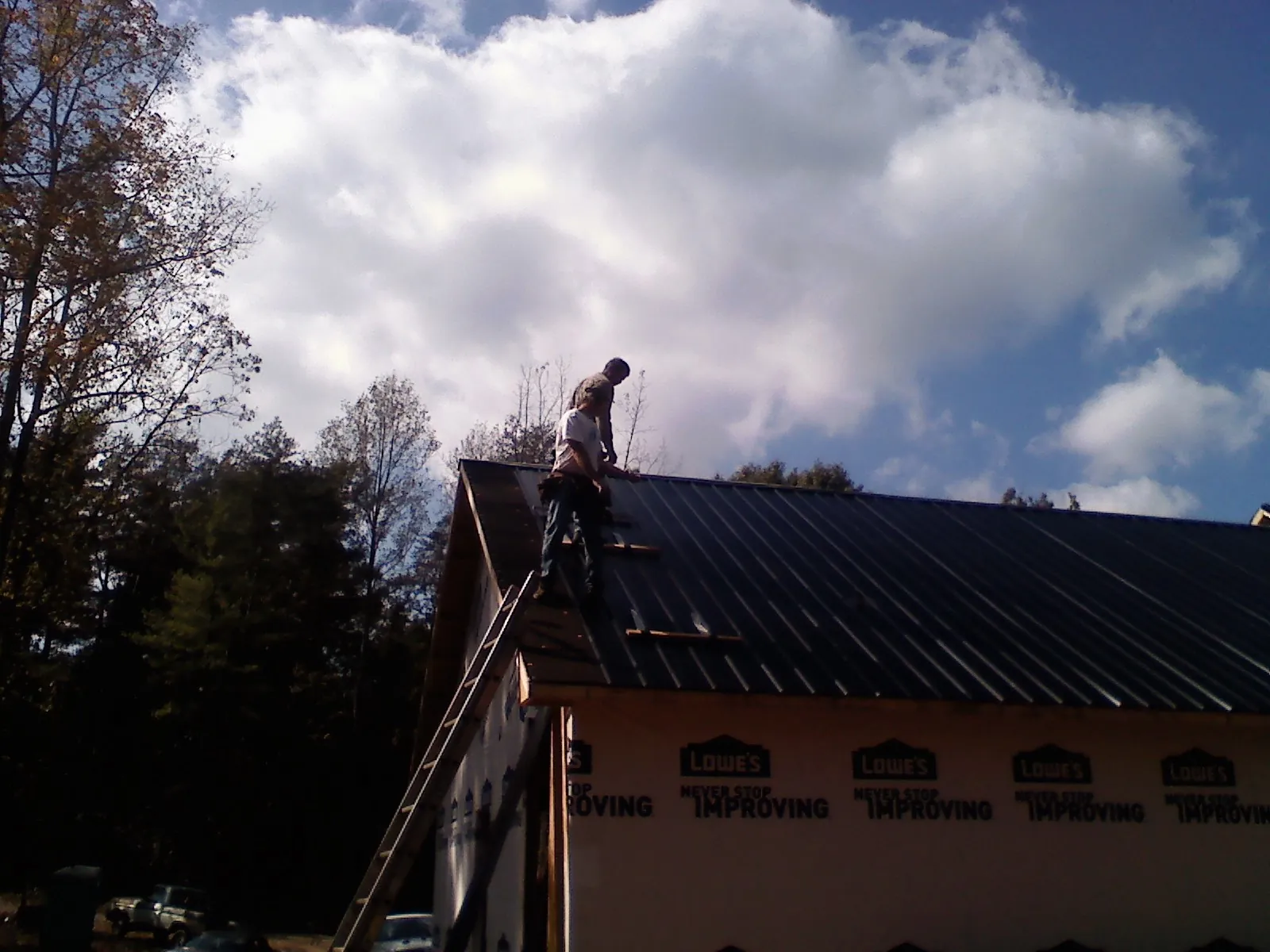 Roofer fastening dark metal panels high against a cloudy sky, from a Roof Inspection job in Allyn