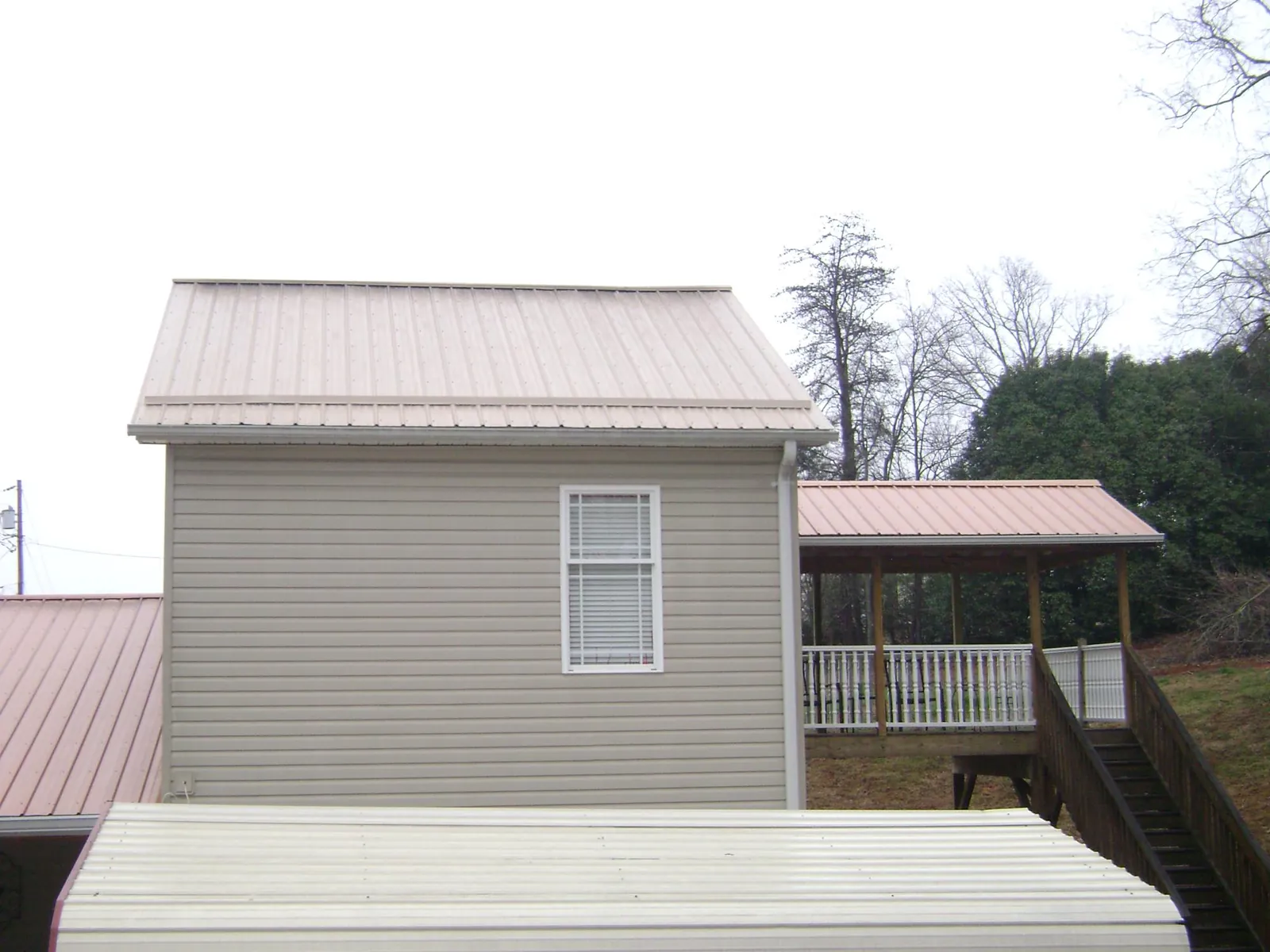 Tan metal roofs on a two story addition and attached porch, from a Roof Replacement job in Allyn