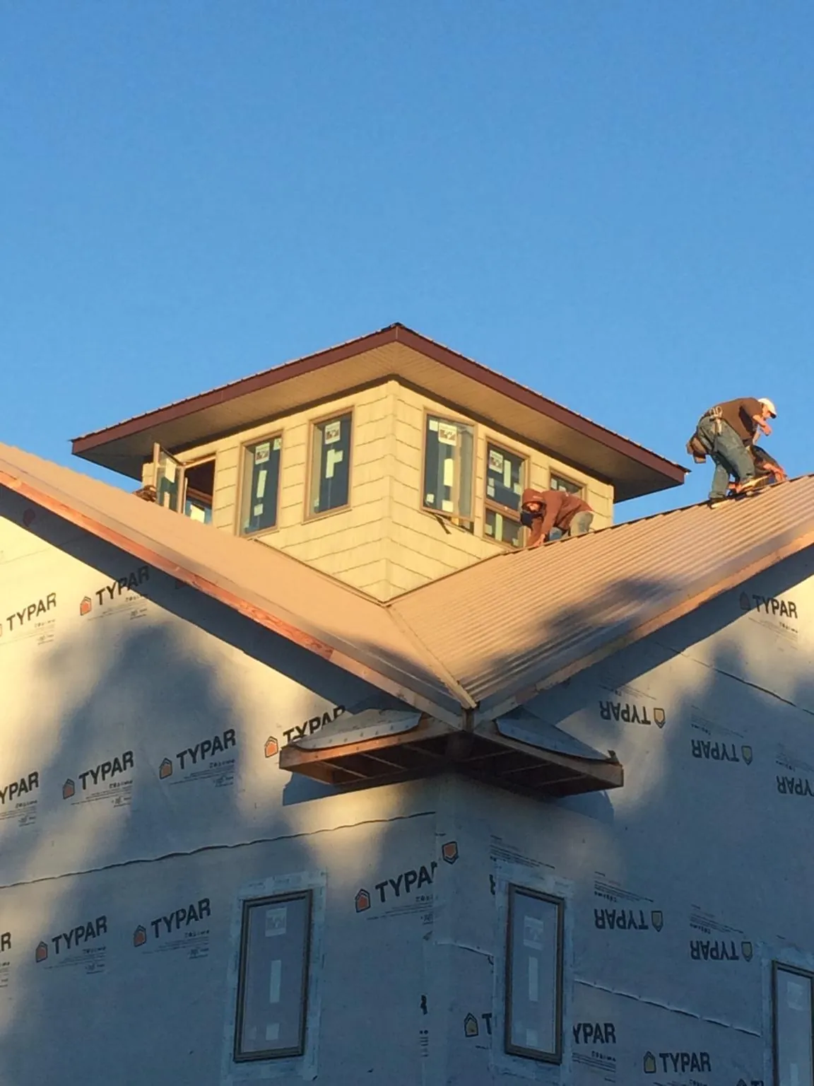 Roofers working around a rooftop cupola on a new metal roof at sunset in Allyn